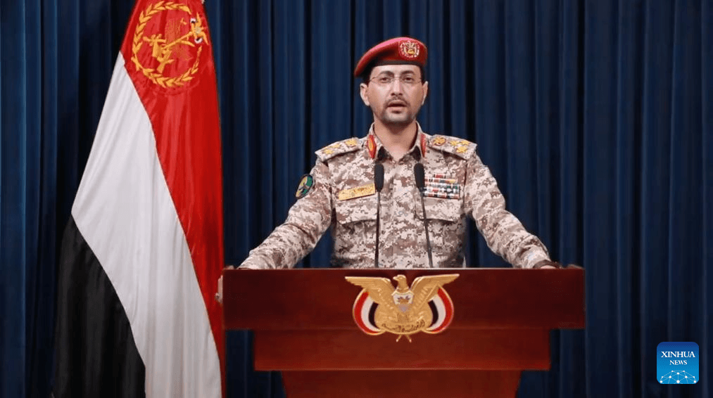 A Houthi military official addressing the media in front of a Yemeni flag