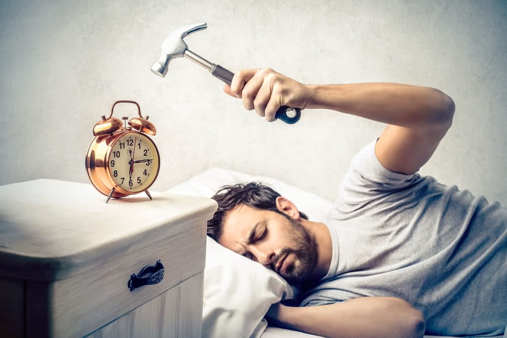 Person struggling to wake up early after a time change, looking at an alarm clock